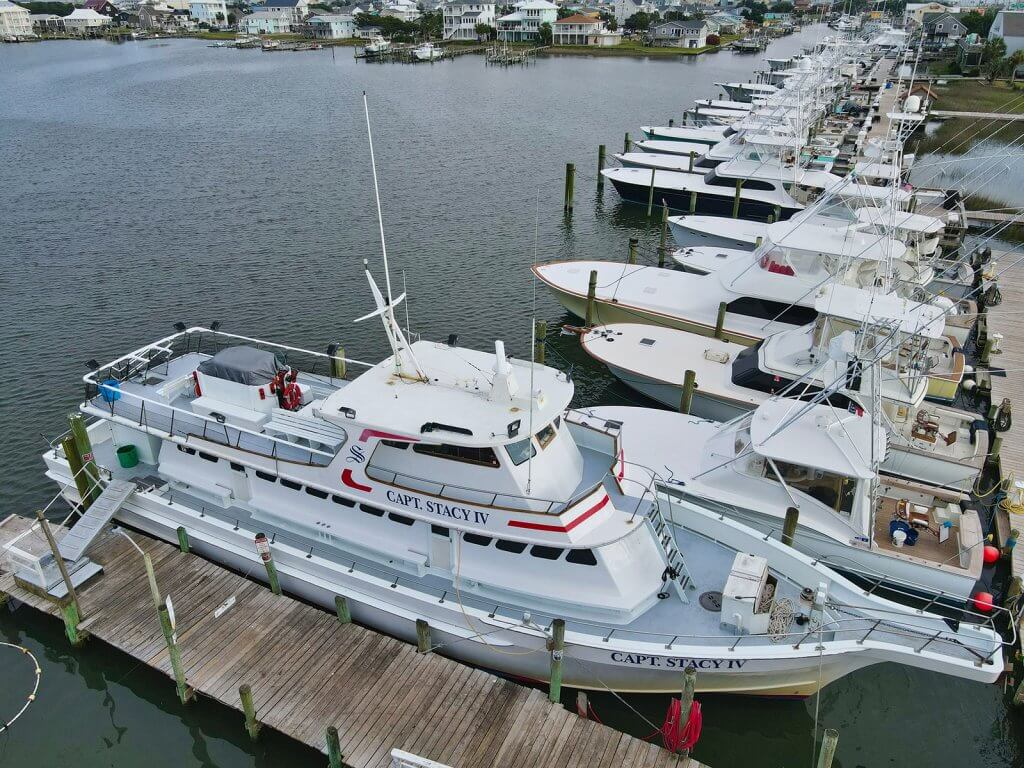 Iz zraka snimljena flota charter ribarskih brodova privezanih uz drvene gatove u marini uz obalno naselje.