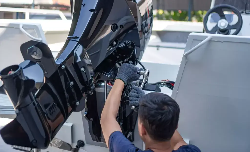 Serviser u rukavicama ključem radi na crnom motoru na krmi manjeg plovila tijekom servisa motora.