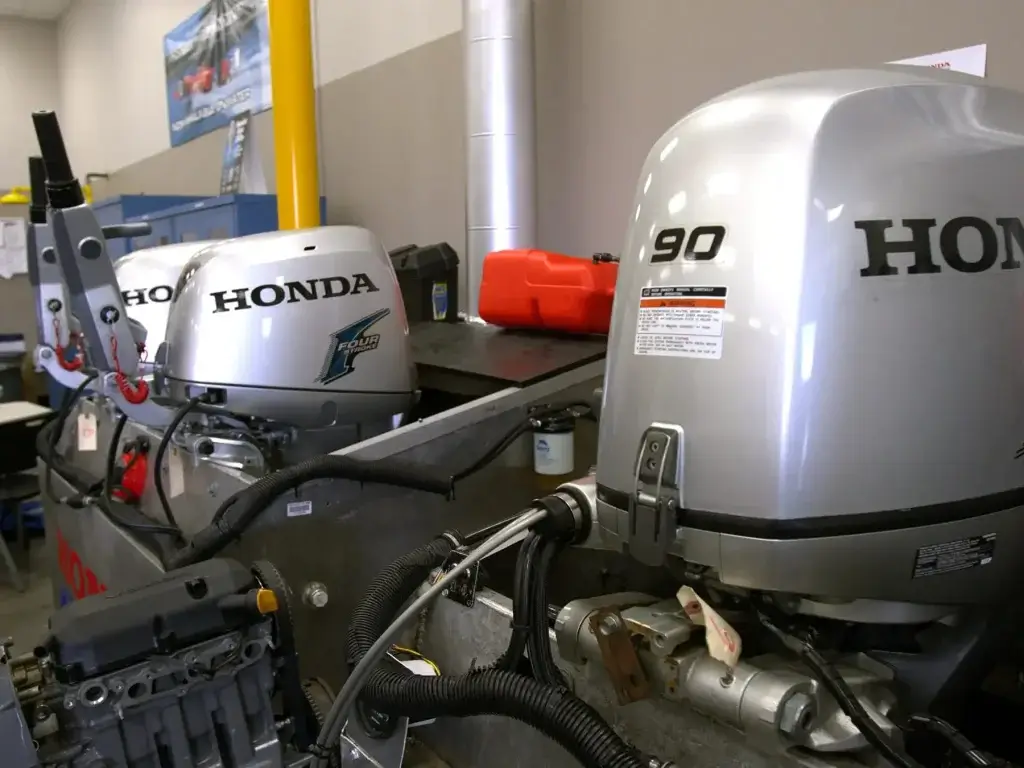 Dva srebrna Honda vanbrodska motora, jedan s oznakom 90, rastavljena na radnom stolu u servisnoj radionici.