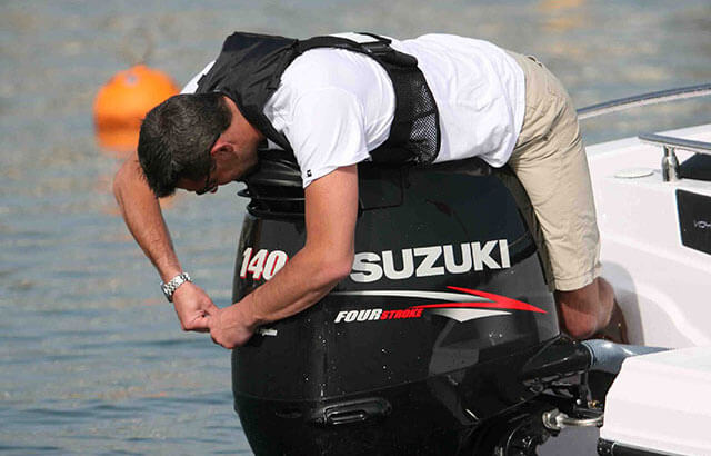 Muškarac u prsluku radi na crnom Suzuki 140 Fourstroke vanbrodskom motoru na krmi plovila.